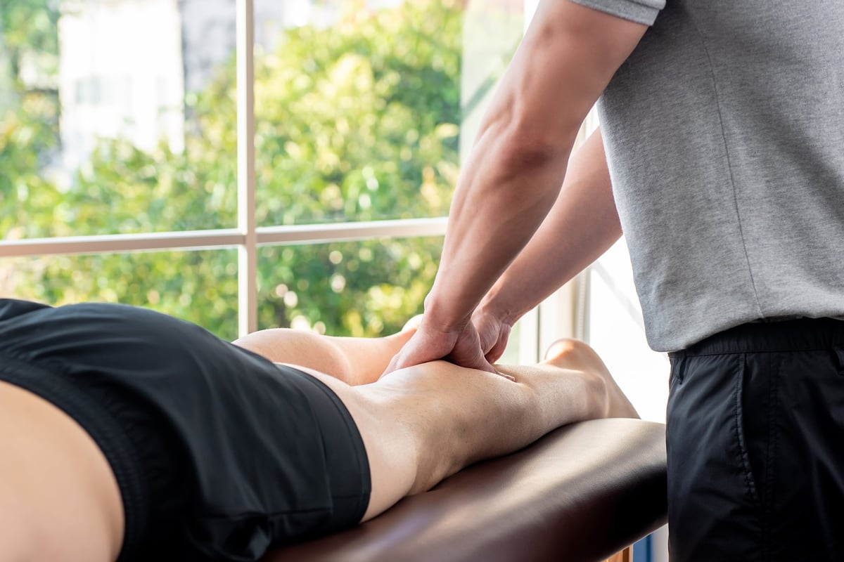 A male therapist giving a leg massage to an athlete patient on a clinic bed