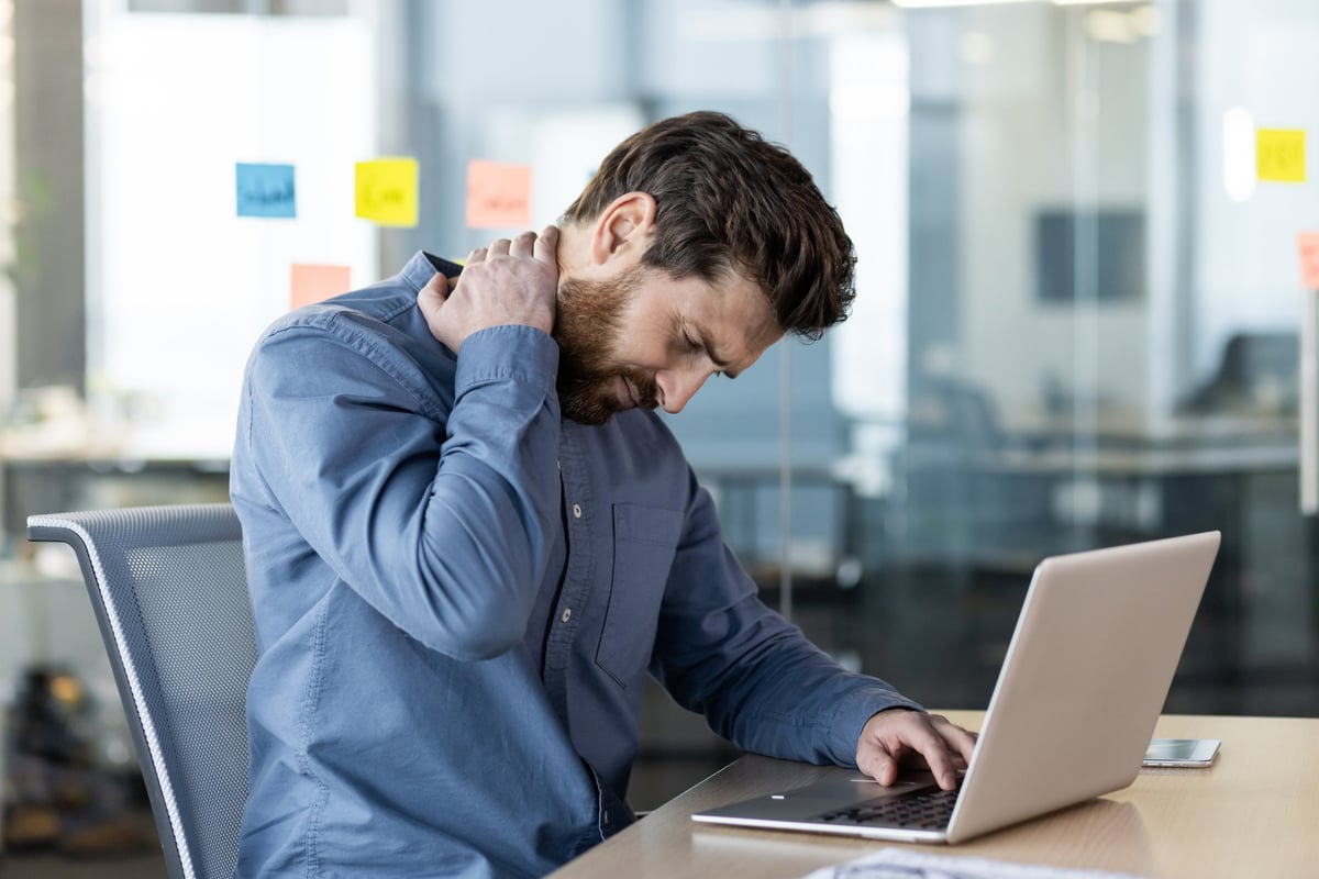 A tired man holding his stiff neck while working at a desk
