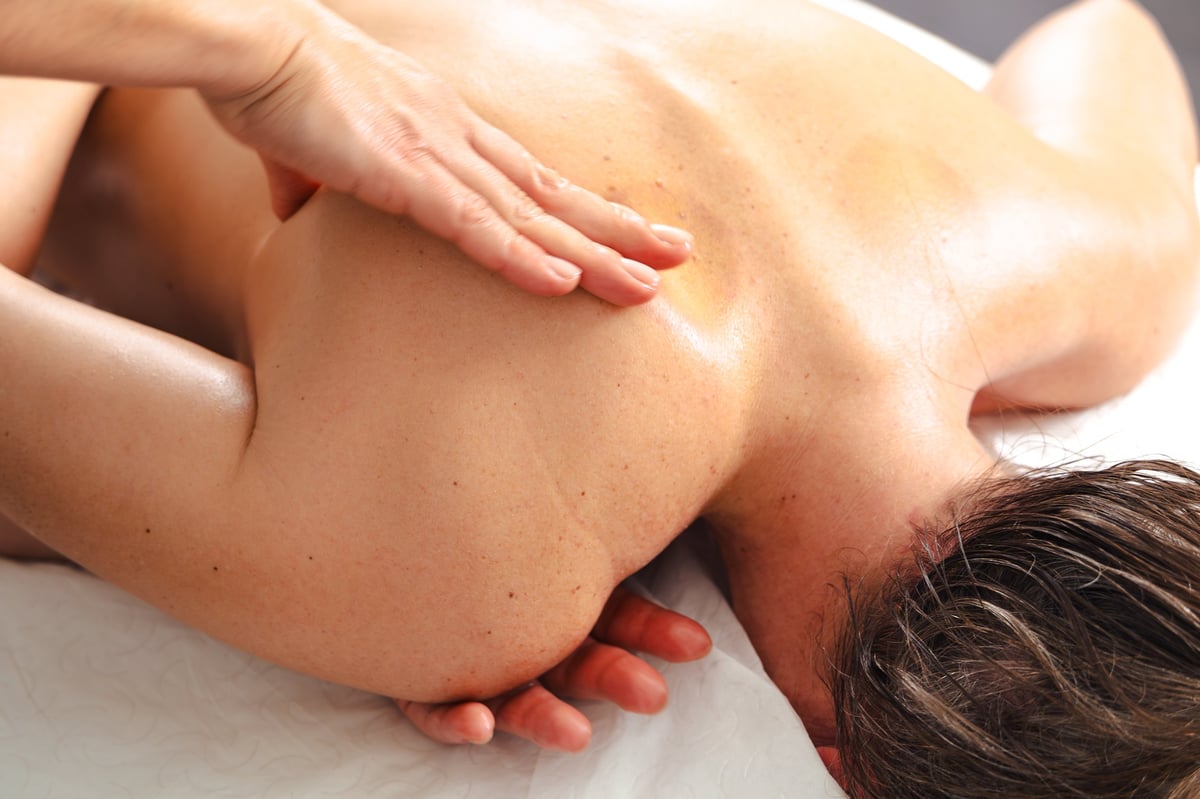 A massage therapist performing deep tissue shoulder massage on a client
