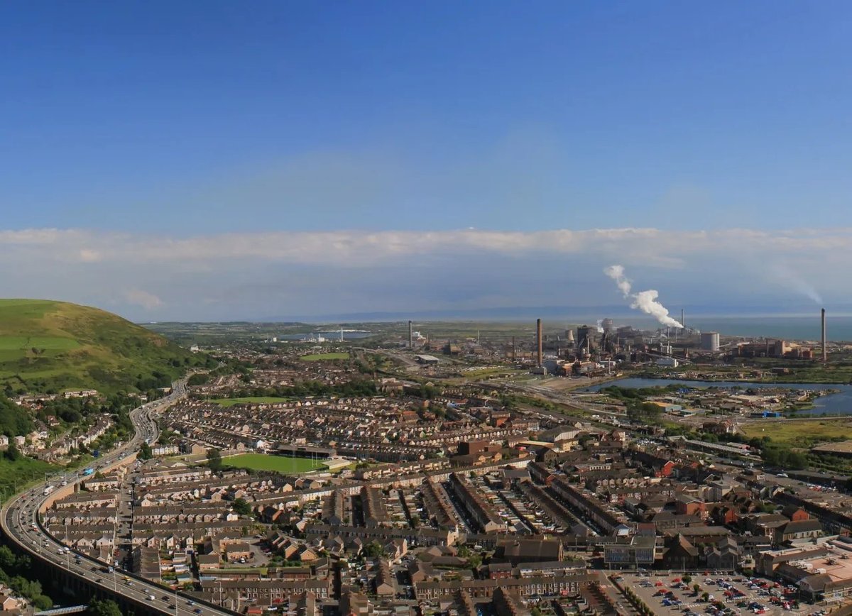 Aerial view of industrial city with residential neighborhoods, factory smokestacks, and green hills in the background